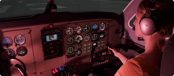 A female aviation student sits in the pilots seat and inspects the various instruments of the aircraft.